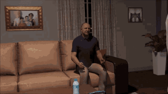 a man sits on a couch with a picture of a family on the wall behind him