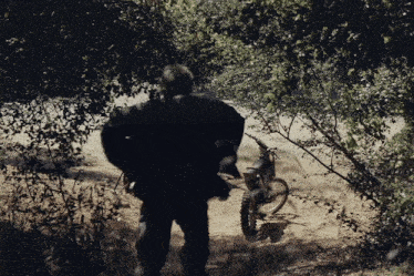 a man in a black jacket is walking in the woods near a dirt bike