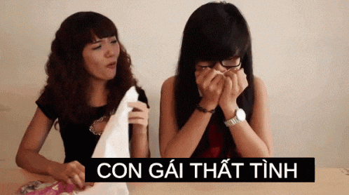 two women sitting at a table with a sign that says con gai that tinh on it