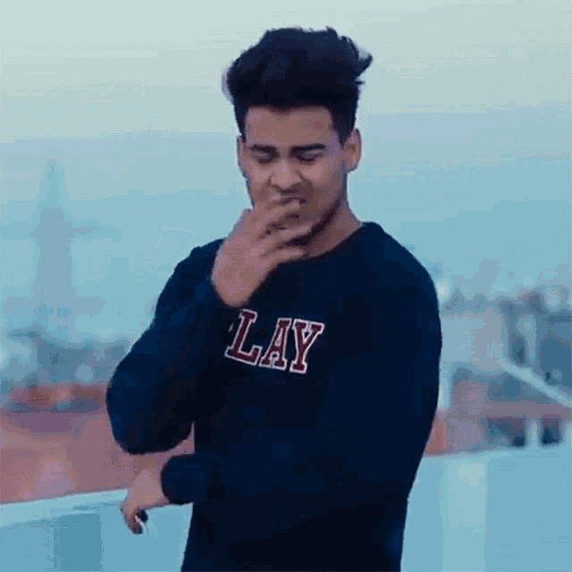 a young man wearing a lay sweatshirt is covering his mouth with his hand