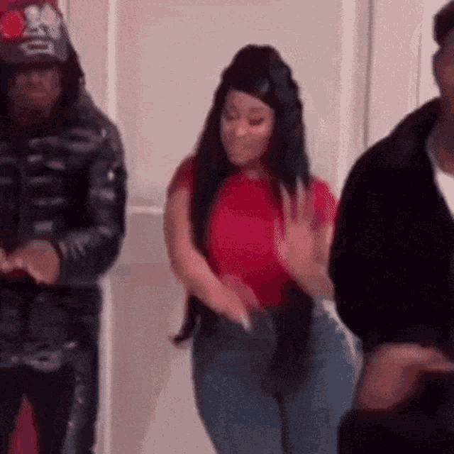 a woman in a red shirt and blue jeans is dancing with two men .
