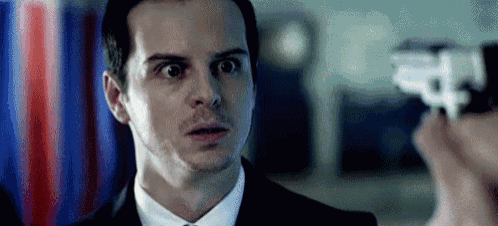 a man in a suit is looking at a person holding a gun .