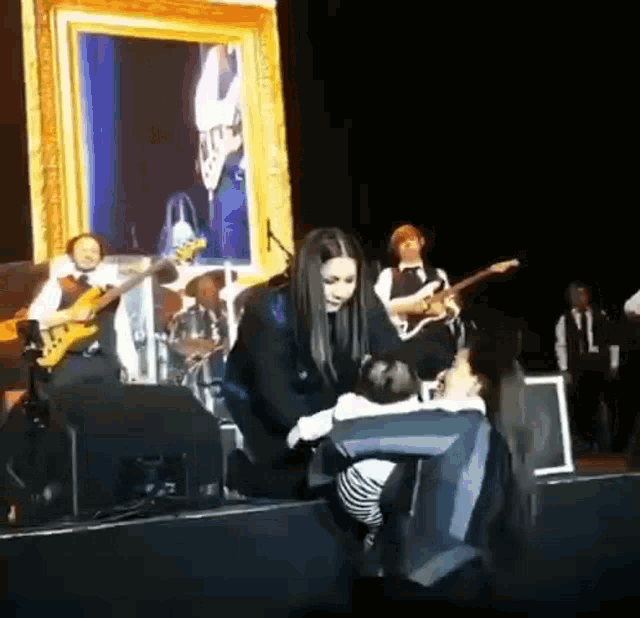 a woman is holding a baby on a stage while a band plays behind her .