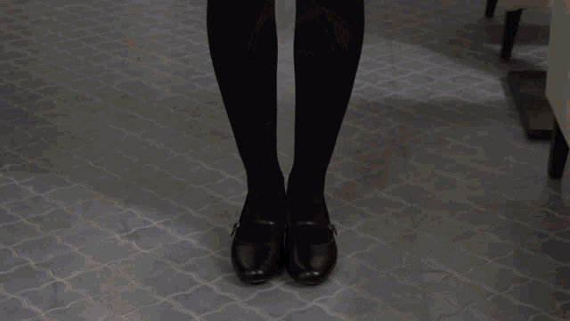 a woman in a black skirt and black tights is standing in a room