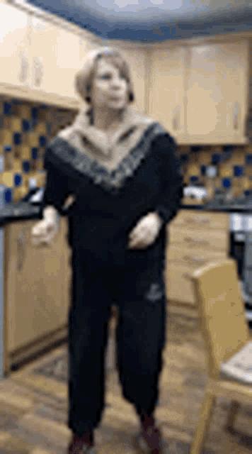 a woman is standing in a kitchen wearing a scarf and a black sweater .