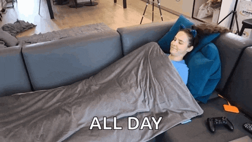 a woman is laying on a couch wrapped in a blanket with the words all day above her .