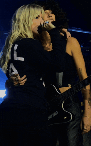 a woman holding a microphone next to a woman holding a guitar that says emma bird