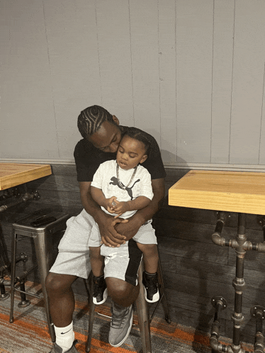 a man sitting on a stool holding a little boy who is wearing a puma shirt