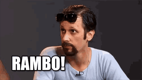 a man with a beard wearing sunglasses and a light blue shirt says rambo