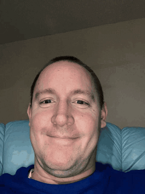 a man in a blue shirt smiles while sitting on a couch