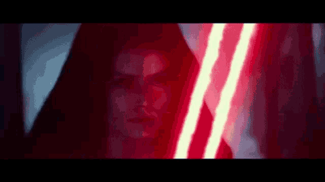 a woman in a black hood is holding a red lightsaber .