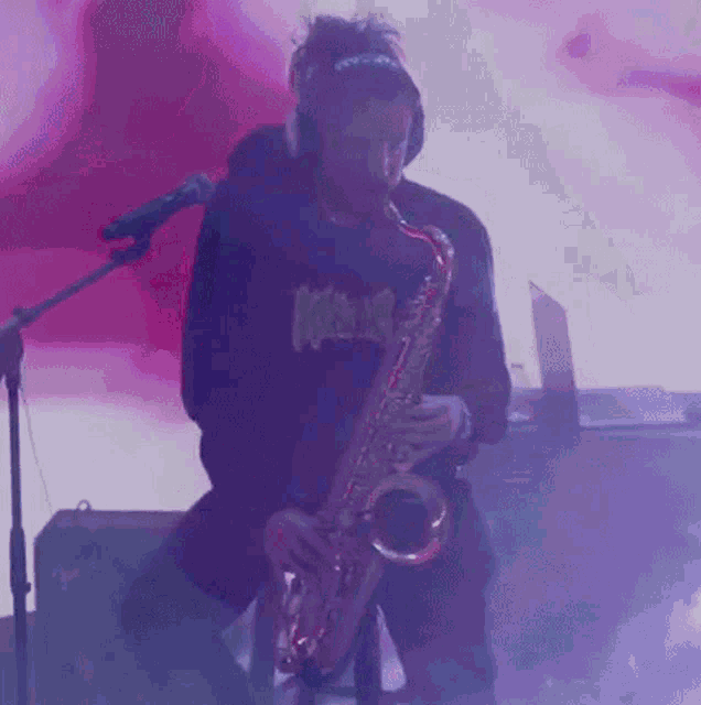 a man wearing headphones is playing a saxophone in front of a pink background .