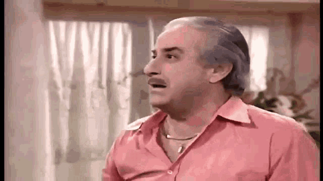 a man with gray hair and a mustache is wearing a pink shirt and making a funny face .