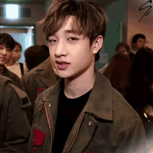 a young man wearing a green jacket and earrings is standing in a crowd .