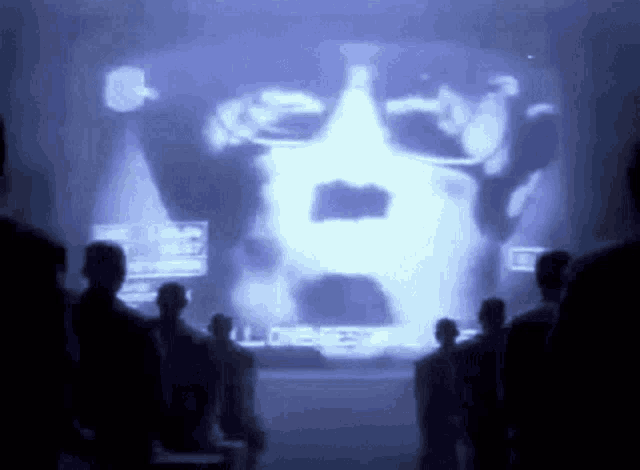 a group of people are standing in front of a screen with a picture of a man 's face on it