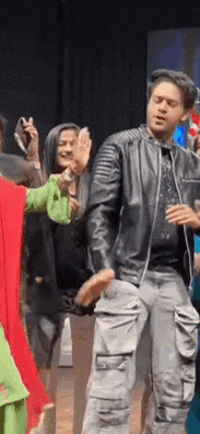 a man in a black leather jacket is dancing with a group of people .