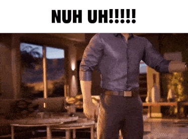 a man in a blue shirt is standing in a living room with the words nuh uh !!!