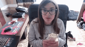 a woman wearing glasses is sitting in a chair eating a sandwich