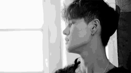 a black and white photo of a young man leaning against a wall and looking at the camera .