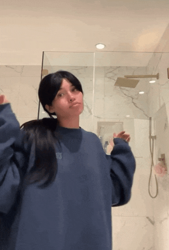 a woman in a blue sweatshirt stands in front of a shower