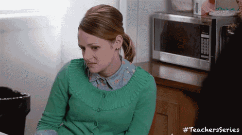 a woman is sitting in front of a microwave in a kitchen .