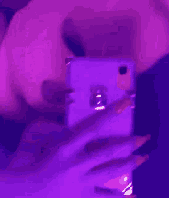 a woman is taking a selfie with her cell phone in a purple light .
