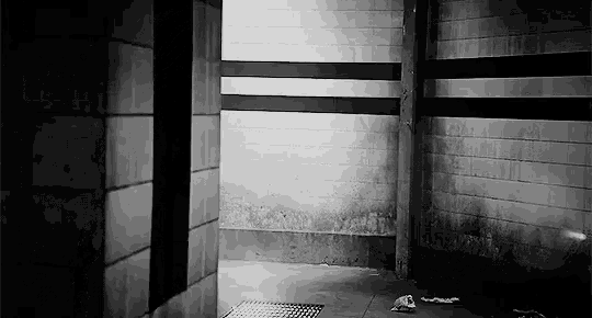 a black and white photo of a dark room with a brick wall and a drain .