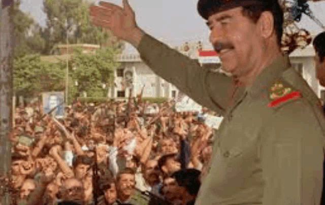 a man in a military uniform is standing in front of a crowd of people and waving .