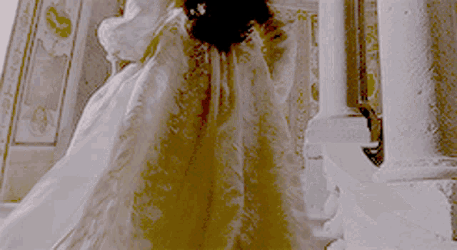 a woman in a white and gold dress is standing on stairs