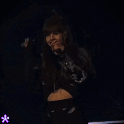 a woman in a black jacket is dancing on a stage with a purple star in the background