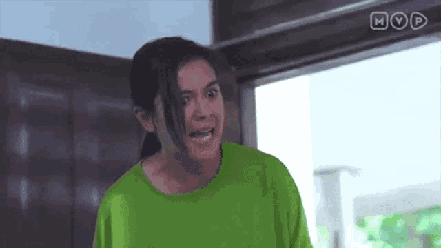 a woman in a green shirt is standing in front of a door and making a funny face .