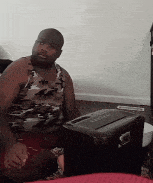 a man wearing a camo tank top sits in front of a shredder