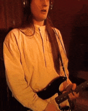 a man with long hair is wearing headphones and playing an electric guitar