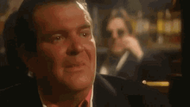 a man in a suit and tie is sitting at a table in a bar looking at something .