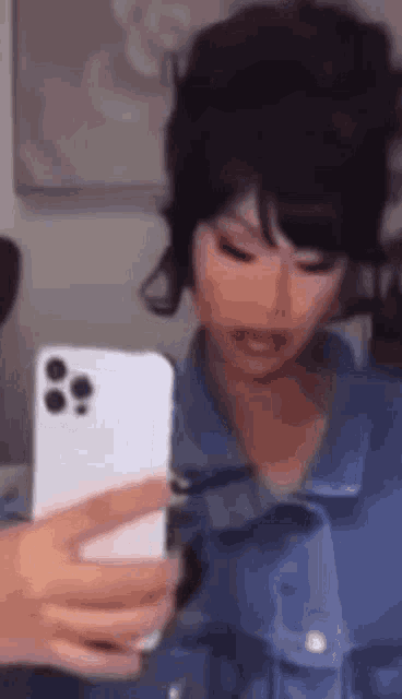 a woman in a denim jacket is taking a selfie with her phone .