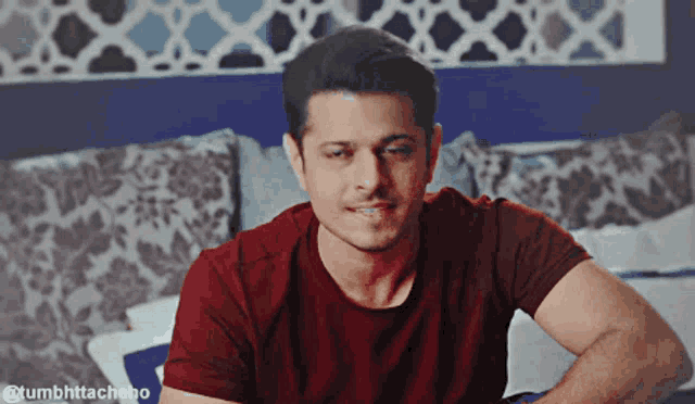 a man in a red t-shirt is sitting on a bed
