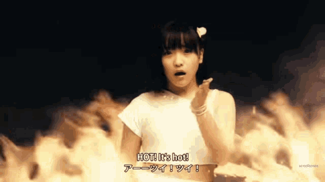a girl in a white shirt says hot it 's hot in front of flames
