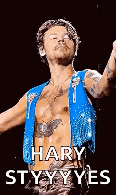 harry styles is wearing a blue vest and holding a microphone .