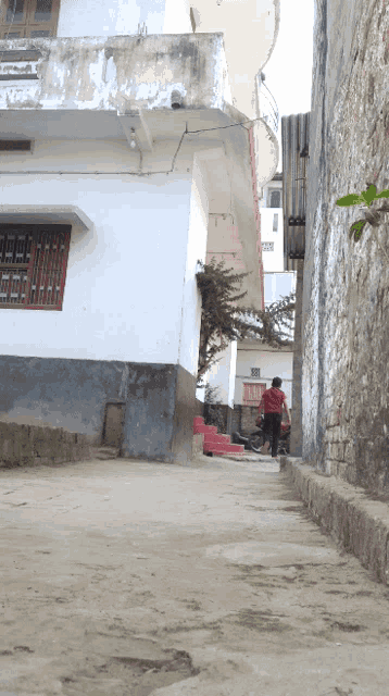 a man in a red shirt walks down a narrow street between two buildings