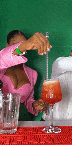 a woman in a pink top stirs a drink in a glass