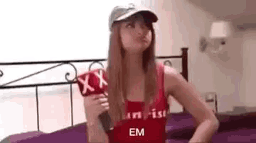 a woman in a red tank top and a hat is holding a microphone in front of a bed .