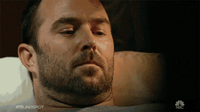 a man with a beard is laying in a bed with the nbc logo in the corner