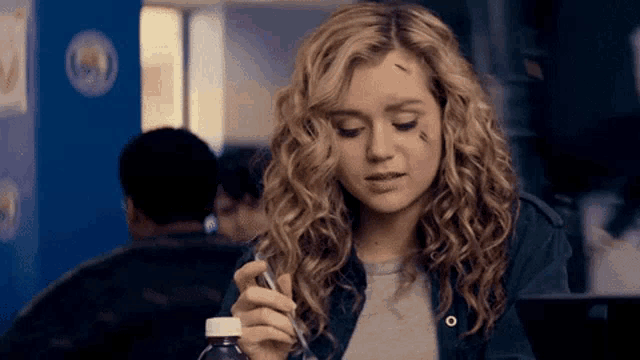 a woman with curly hair is holding a bottle of liquid and a spoon .