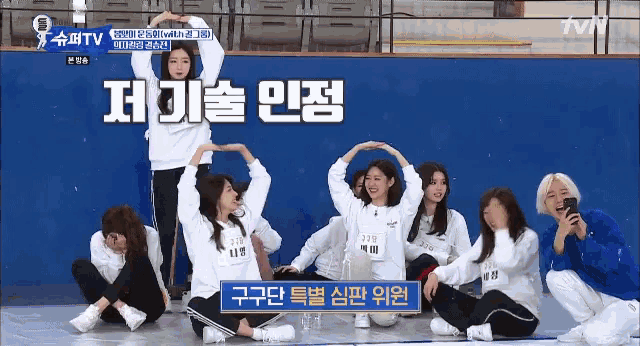 a group of girls are sitting on the floor with their arms outstretched in front of a blue wall with tvn written on it