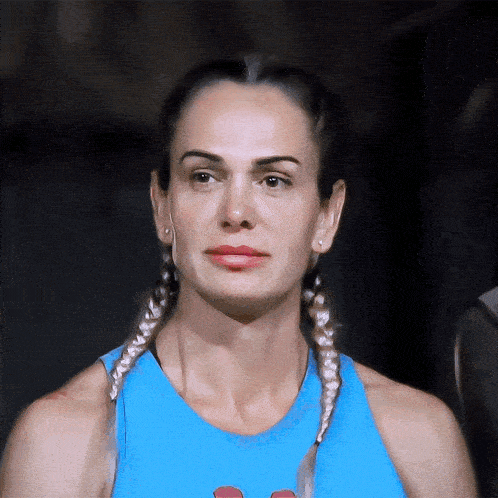 a woman with braids wearing a blue tank top looks at the camera