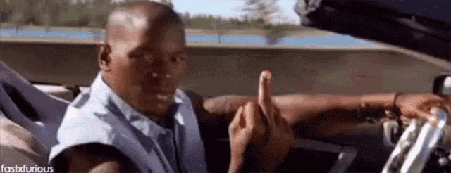 a man is sitting in a car and giving the middle finger .
