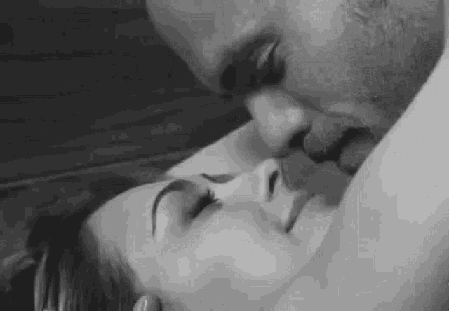 a black and white photo of a man kissing a woman on the neck .