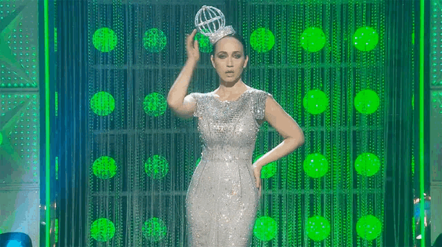 a woman in a silver dress is holding a crown in her hand .