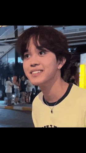 a young man wearing a yellow shirt and a black necklace smiles