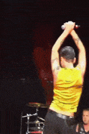 a man in a yellow shirt is singing into a microphone with his arms in the air